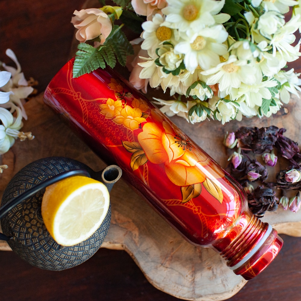 botella de agua de cobre naranja con flores y una rodaja de limón
