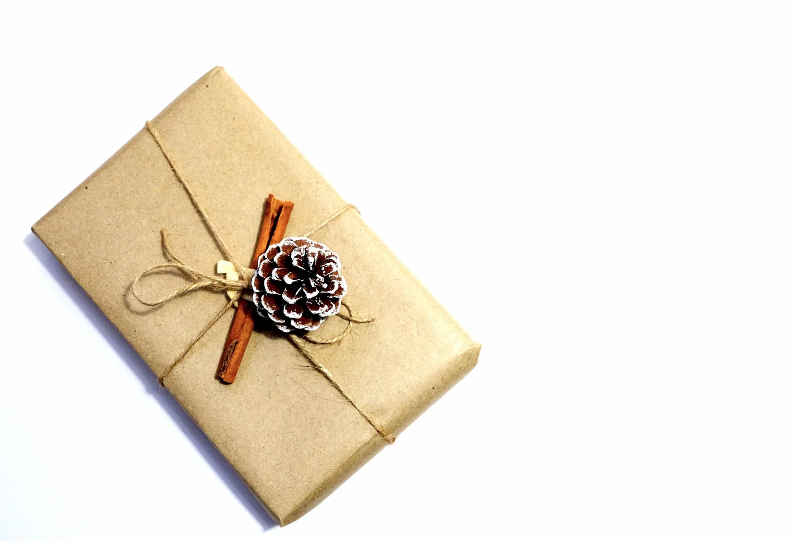 regalo envuelto con papel marrón con ramita de canela y piña de un pino